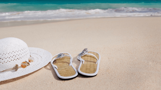 A hat and flip-flops on the beach- Beach Vacation Packing List.