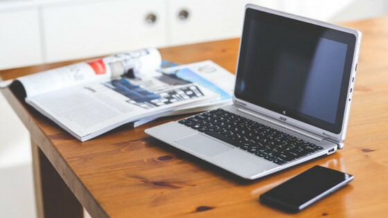 Laptop, cell phone and magazines on a table.